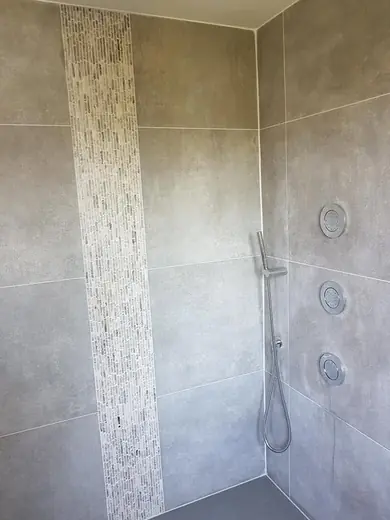 Espace douche carrelé gris avec buses hydromassantes et bande de mosaïque