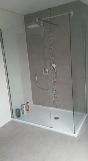 Douche avec paroi en verre, receveur blanc et murs revêtus de carrelage gris